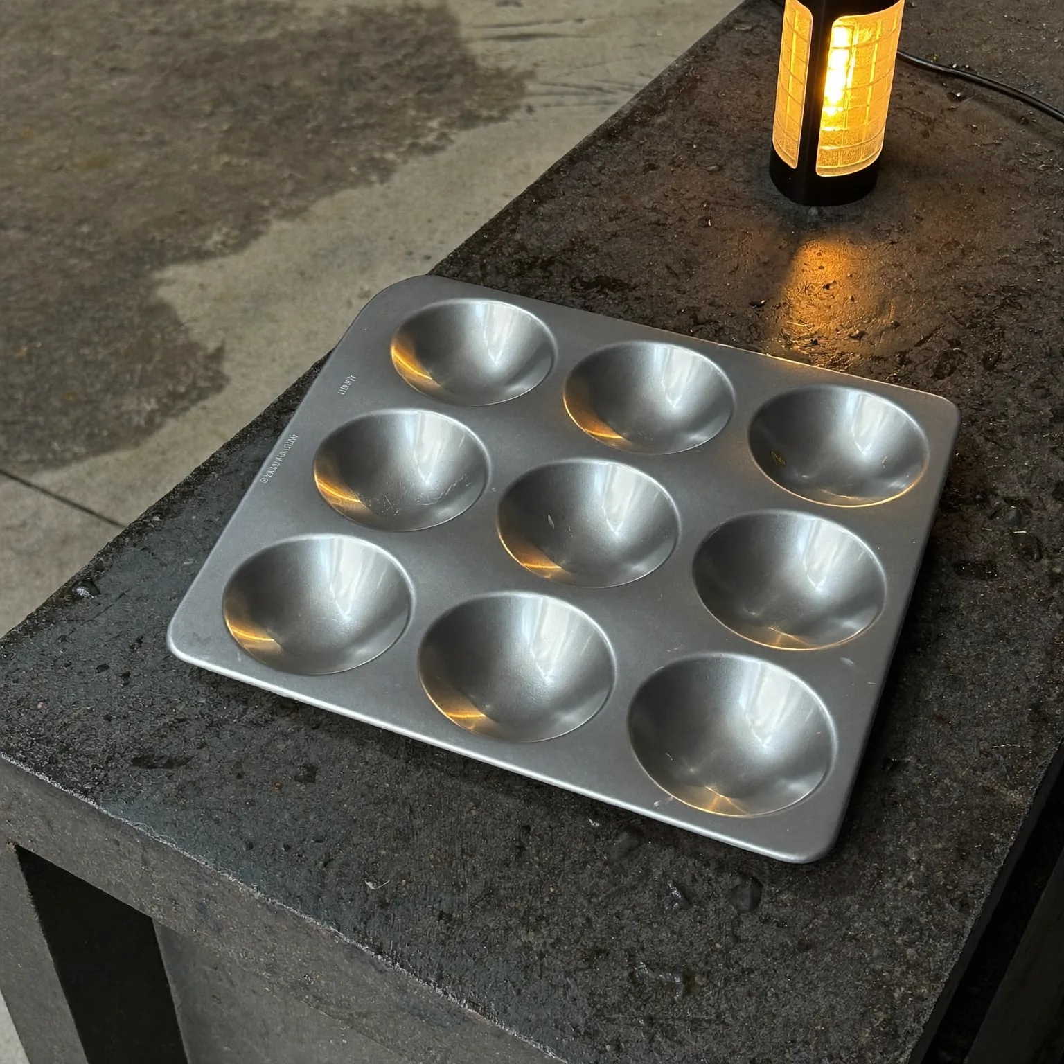 a steel developing tray on a wet concrete bench, amber safelight raking across the surface, quiet mood