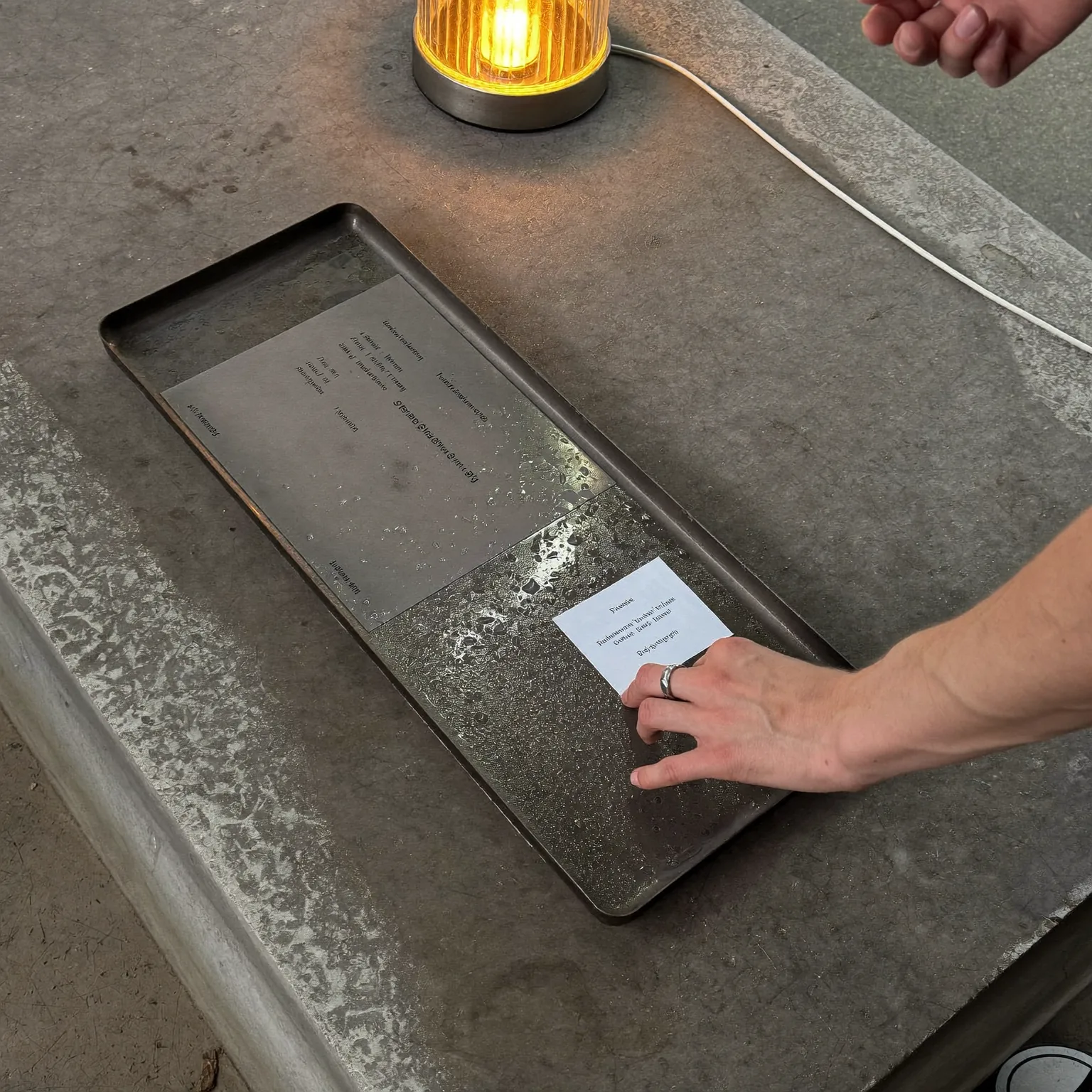 a steel developing tray on a wet concrete bench, amber safelight raking across the surface, quiet mood